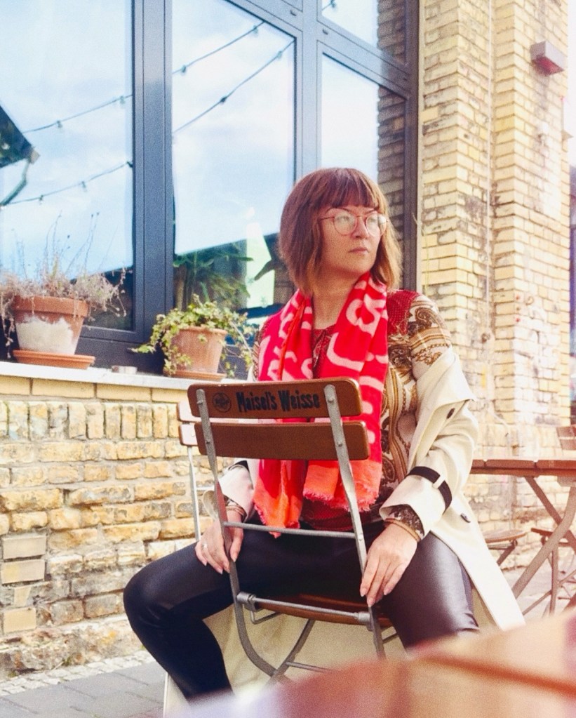 Nath im Café, sitzt rittlings auf einem Holzklappstuhl